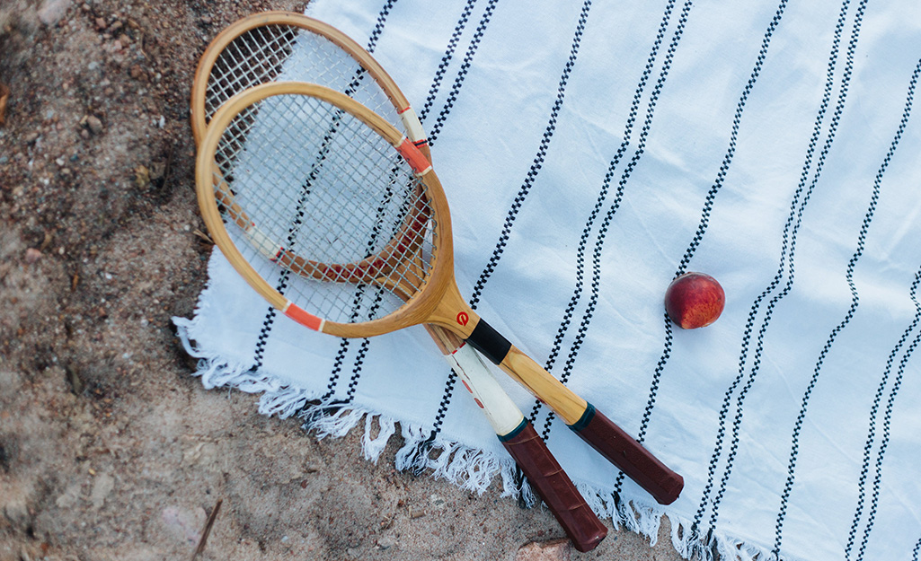Två tennisrack och en boll som ligger på en filt utomhus i naturen.