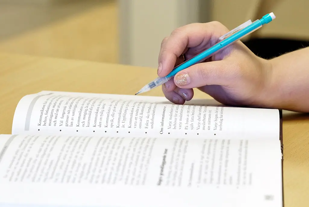 En person som håller i en penna vid en öppen bok. Foto: Tina Engström