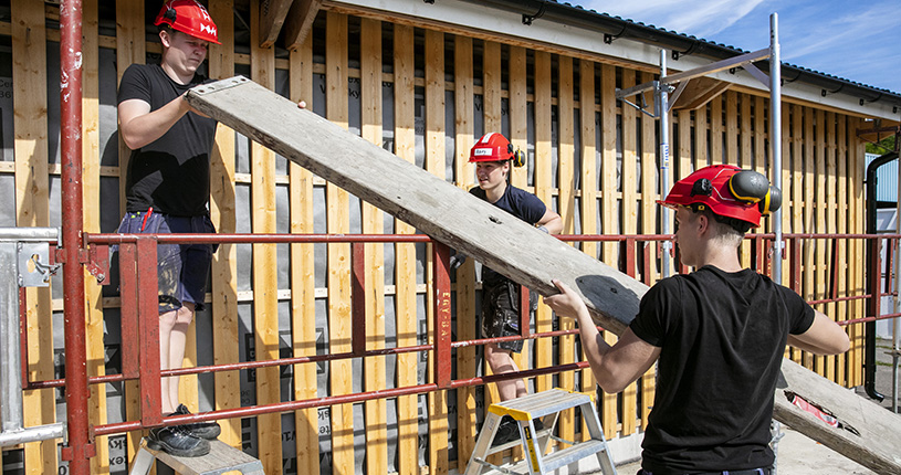 Foto på elever på bygg- och anläggningsprogrammet som lyfter plank.