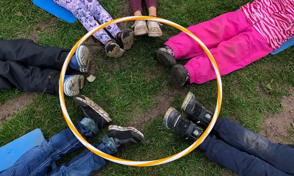 Elever ligger på marken med fötterna i en rockring.