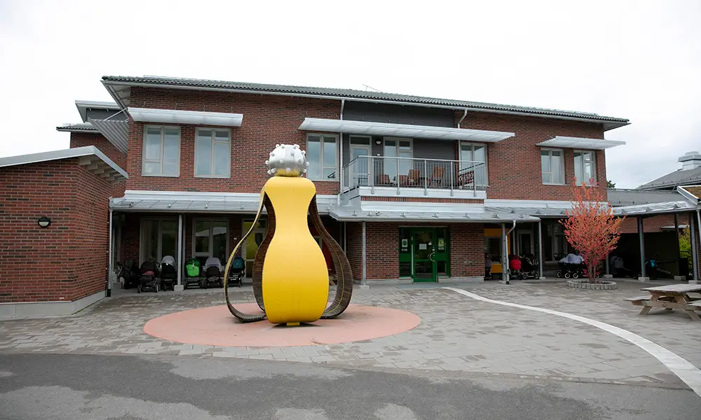Foto på Åkersbergs förskola. Det är en flervåningsbyggnad i tegel. Framför byggnaden finns en gul skulptur. 