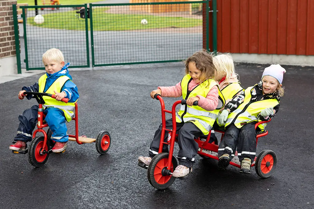 Foto på barn som åker på trehjulingar på skolgården.
