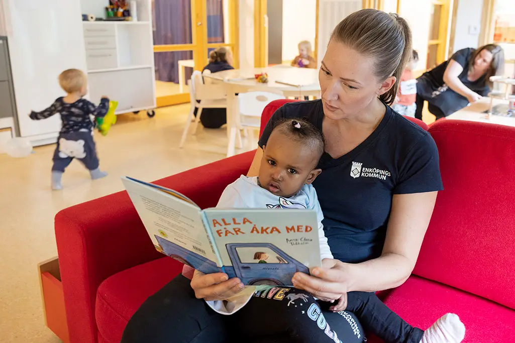 Foto på en kvinnlig pedagog som läser för ett litet barn.
