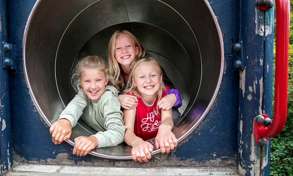 Foto på tre elever som ligger i en tunnel och ler mot kameran.